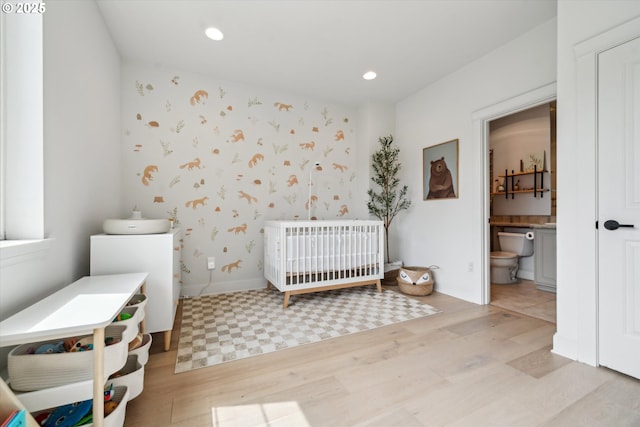 bedroom featuring recessed lighting, light wood-style flooring, ensuite bath, and a crib