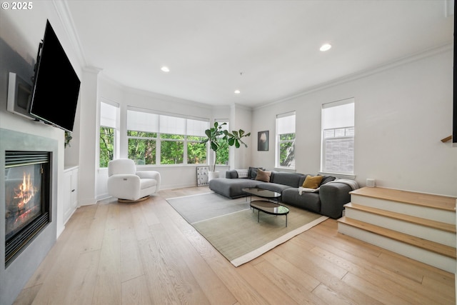 living room featuring crown molding, wood-type flooring, a glass covered fireplace, recessed lighting, and baseboards