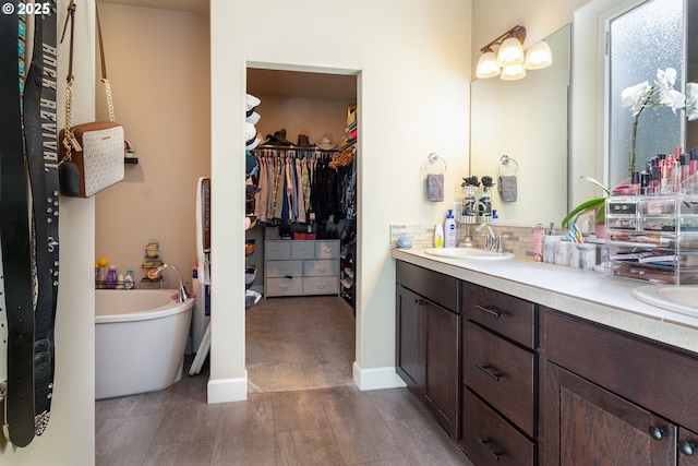 bathroom featuring double vanity, baseboards, a spacious closet, a freestanding tub, and a sink