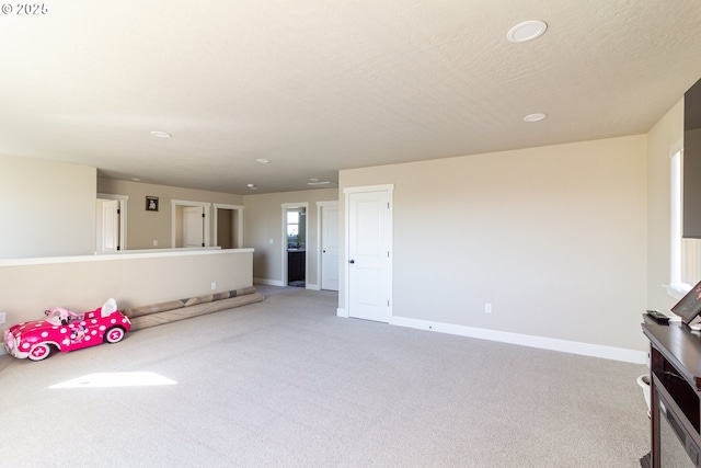 unfurnished living room with light colored carpet, a textured ceiling, and baseboards