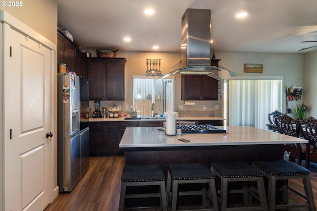 kitchen with dark brown cabinetry, island range hood, dark wood-style floors, light countertops, and stainless steel refrigerator with ice dispenser