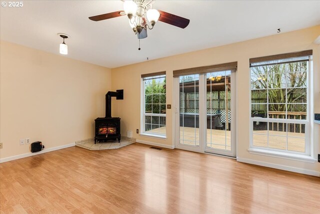 unfurnished living room featuring wood finished floors, baseboards, a wood stove, and visible vents