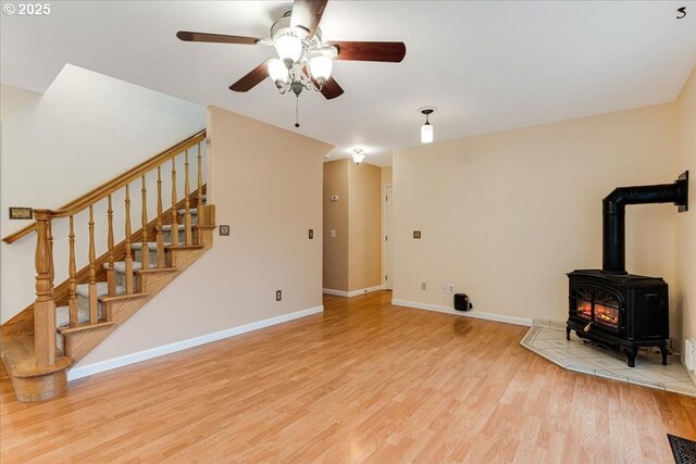living area featuring stairway, a wood stove, baseboards, a ceiling fan, and wood finished floors