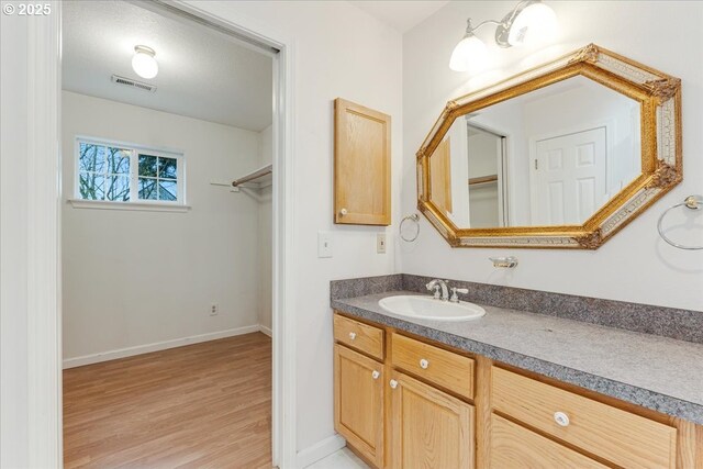 bathroom with baseboards, visible vents, vanity, and wood finished floors