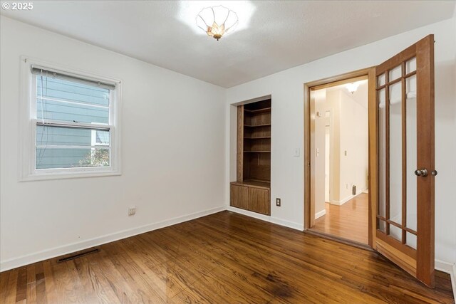 unfurnished bedroom with baseboards, dark wood-style floors, and visible vents