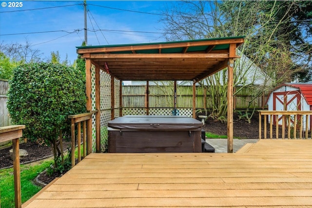 wooden terrace featuring a fenced backyard, an outbuilding, a shed, and a hot tub