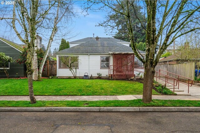 view of front facade featuring a shingled roof, fence, and a front lawn