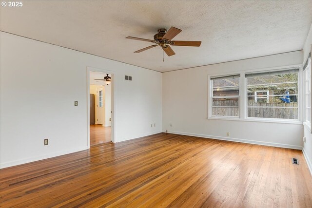 unfurnished room featuring a textured ceiling, visible vents, baseboards, ceiling fan, and hardwood / wood-style floors