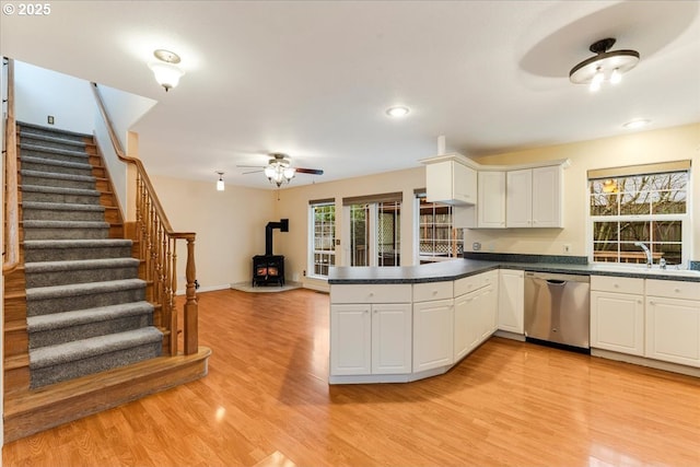 kitchen featuring a wood stove, stainless steel dishwasher, a sink, dark countertops, and a peninsula