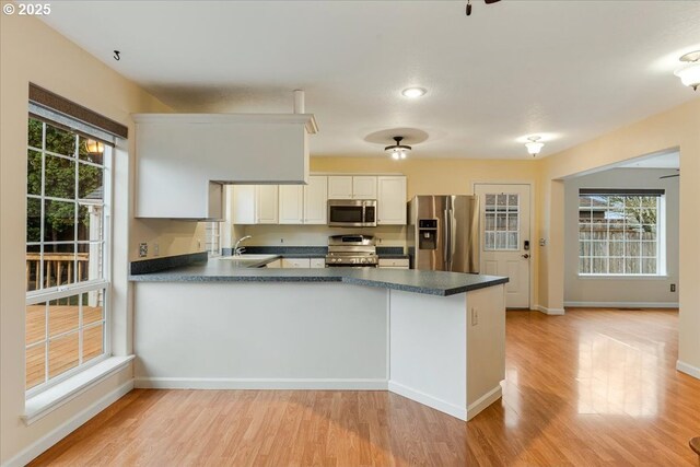 kitchen featuring stainless steel appliances, a sink, dark countertops, light wood finished floors, and a peninsula