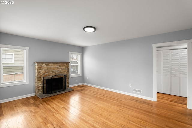 unfurnished living room with visible vents, a stone fireplace, light wood-type flooring, and baseboards