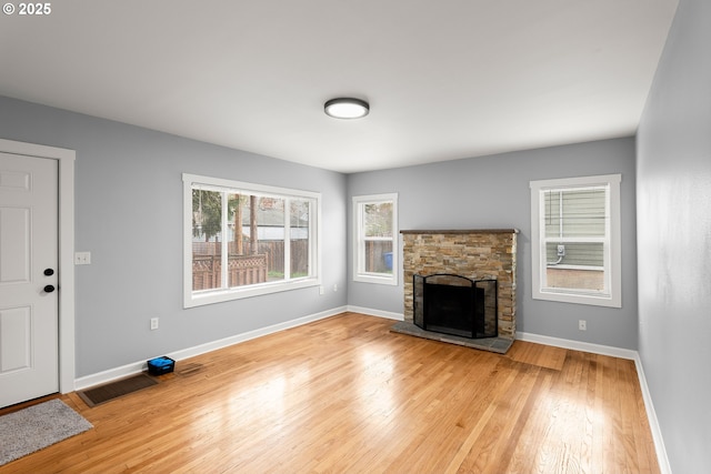 unfurnished living room with visible vents, a stone fireplace, light wood-type flooring, and baseboards