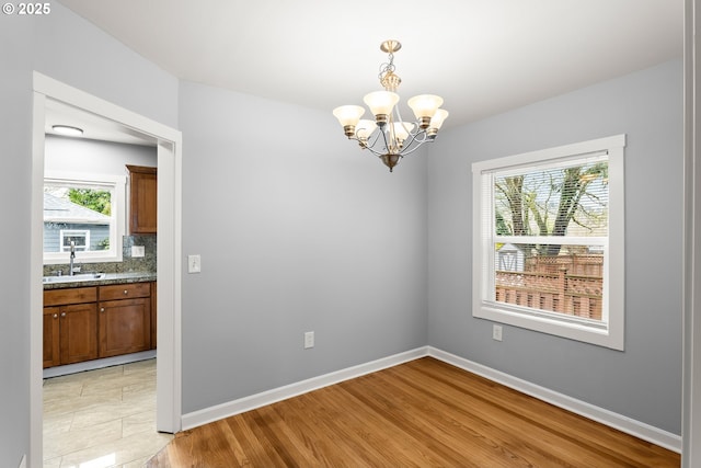 unfurnished dining area with a wealth of natural light, a notable chandelier, light wood-style flooring, and baseboards