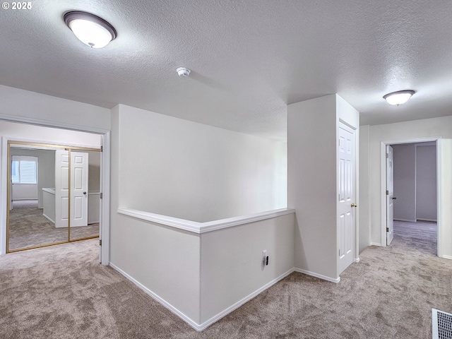 corridor with a textured ceiling, carpet flooring, visible vents, and baseboards