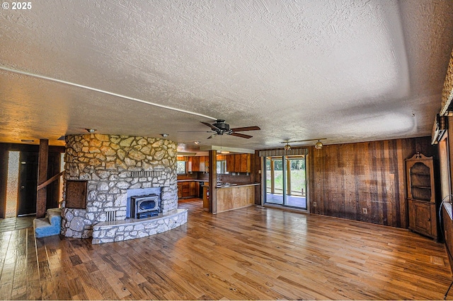 77993 Point Adams Rd, Clatskanie, OR 97016 - unfurnished living room featuring hardwood / wood-style flooring, a textured ceiling, wooden walls, ceiling fan, and a fireplace