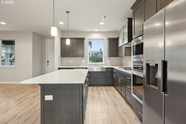 kitchen with a sink, light countertops, light wood-style floors, appliances with stainless steel finishes, and backsplash