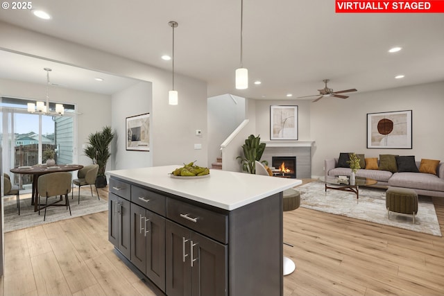 kitchen featuring recessed lighting, a lit fireplace, light countertops, and light wood finished floors