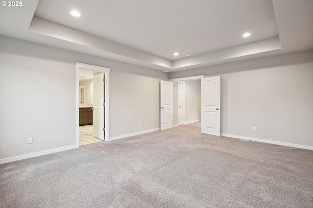 unfurnished bedroom featuring a tray ceiling, light colored carpet, and baseboards