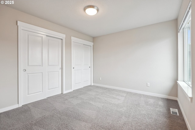 unfurnished bedroom with carpet flooring, baseboards, visible vents, and two closets