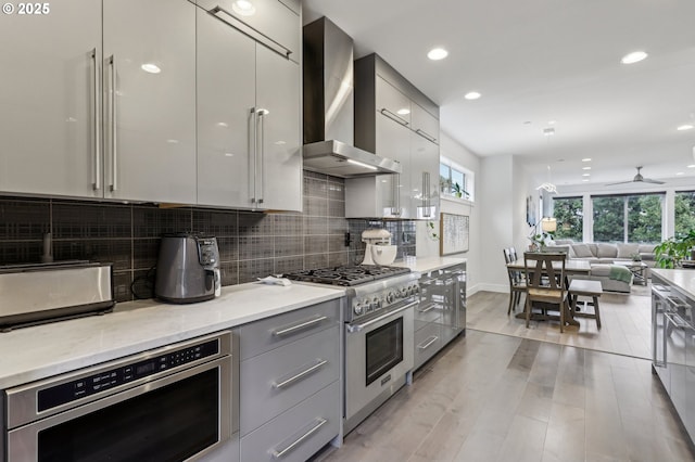 kitchen featuring stainless steel stove, wall chimney range hood, gray cabinetry, and modern cabinets