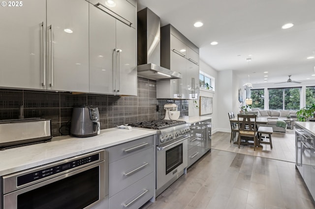 kitchen with modern cabinets, wall chimney range hood, stainless steel appliances, gray cabinets, and recessed lighting