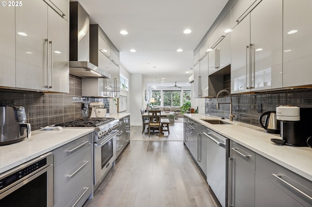 kitchen with gray cabinetry, modern cabinets, wall chimney range hood, stainless steel appliances, and a sink
