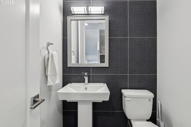 bathroom with toilet, a sink, and tile walls
