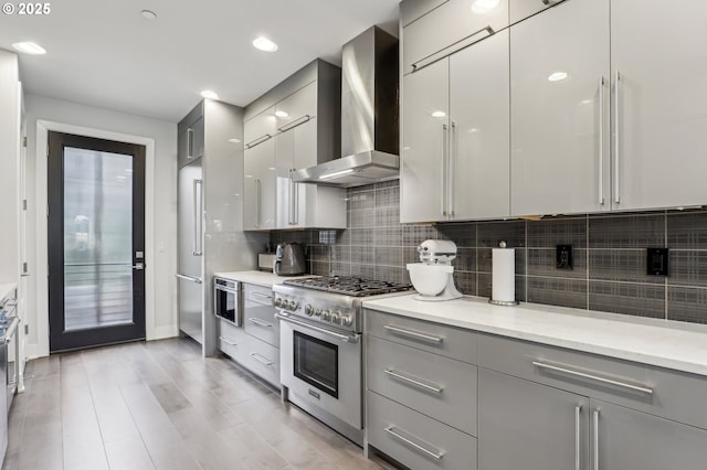 kitchen with high end stove, wall chimney range hood, gray cabinetry, modern cabinets, and decorative backsplash