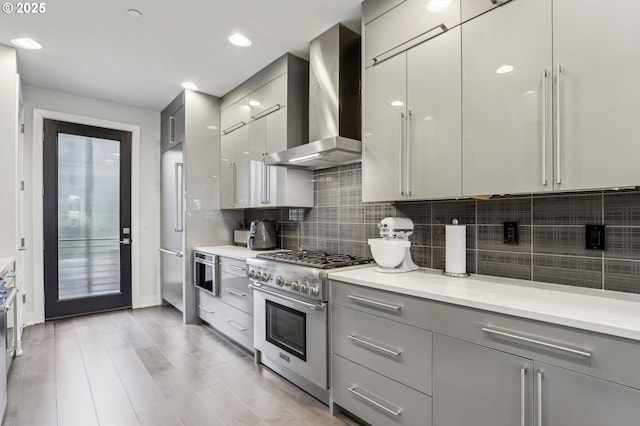 kitchen with decorative backsplash, gray cabinetry, modern cabinets, high quality appliances, and wall chimney exhaust hood