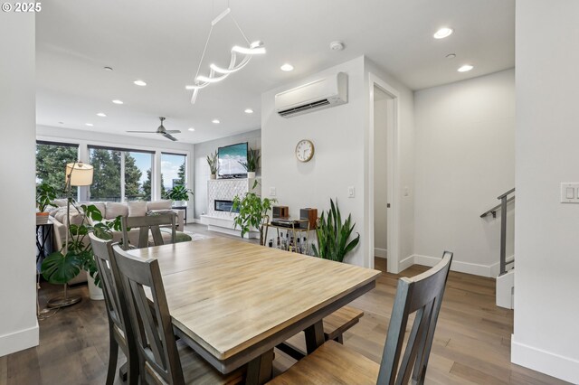 dining space with an AC wall unit, a fireplace, recessed lighting, wood finished floors, and baseboards