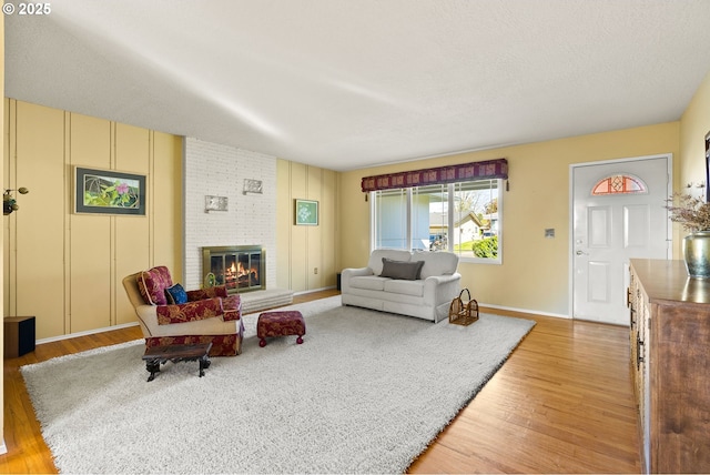 living area featuring baseboards, a brick fireplace, and light wood finished floors