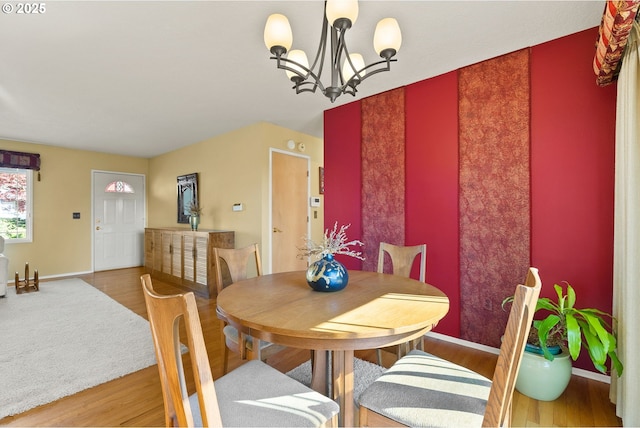 dining room with baseboards, an accent wall, wood finished floors, and a notable chandelier