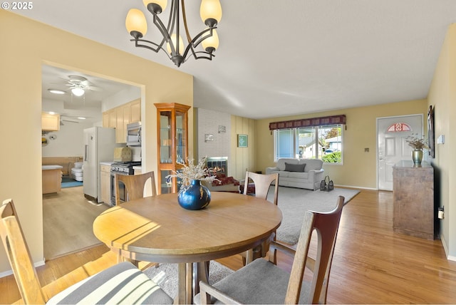 dining area with baseboards, a fireplace, ceiling fan with notable chandelier, and light wood-type flooring