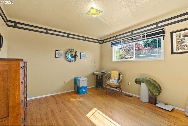 living area featuring a textured ceiling, visible vents, baseboards, and light wood-type flooring