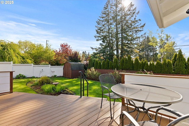 wooden deck featuring outdoor dining space, a storage shed, a fenced backyard, a lawn, and an outdoor structure