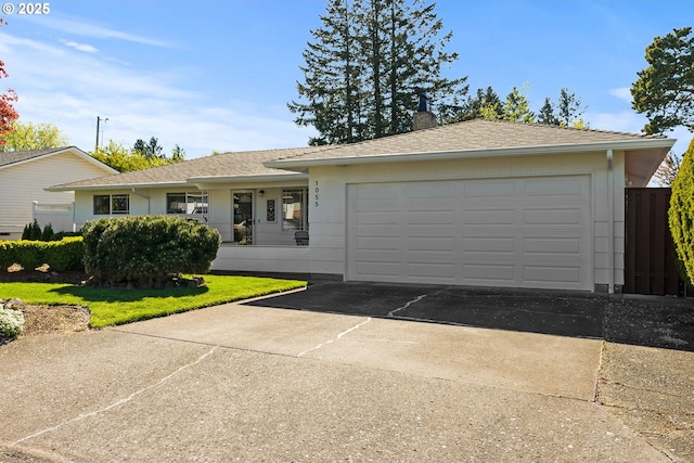 ranch-style home featuring a chimney, a garage, a front lawn, concrete driveway, and a shingled roof
