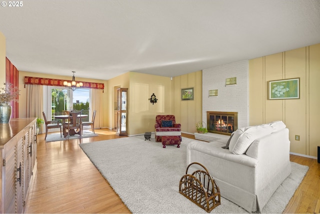 living room featuring an inviting chandelier, baseboards, a brick fireplace, and light wood-type flooring