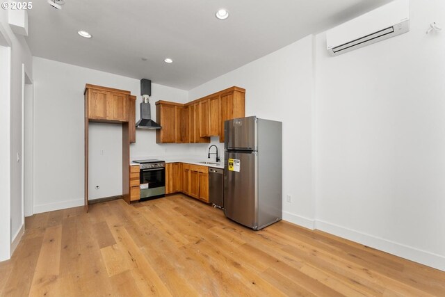 kitchen featuring appliances with stainless steel finishes, a sink, light wood finished floors, wall chimney exhaust hood, and a wall mounted AC