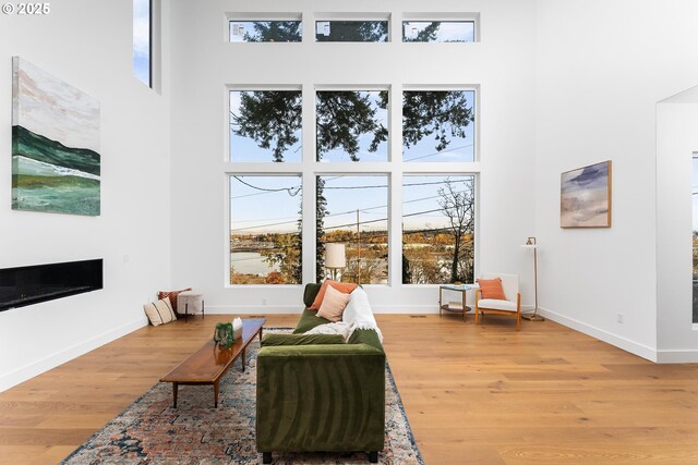 sitting room with a glass covered fireplace, baseboards, a high ceiling, and wood finished floors