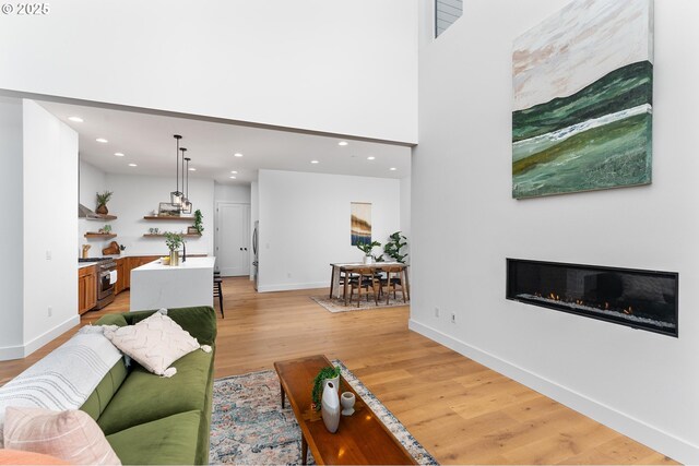 living room featuring recessed lighting, light wood finished floors, a glass covered fireplace, and baseboards
