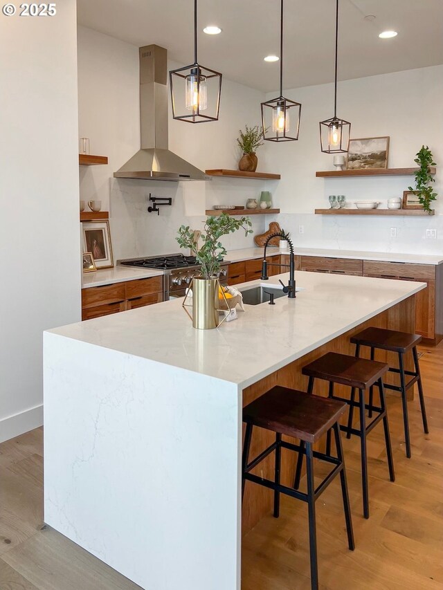 kitchen featuring open shelves, a sink, light wood finished floors, and wall chimney range hood