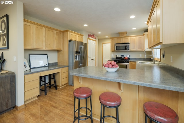 kitchen with light brown cabinetry, a peninsula, stainless steel appliances, and a sink