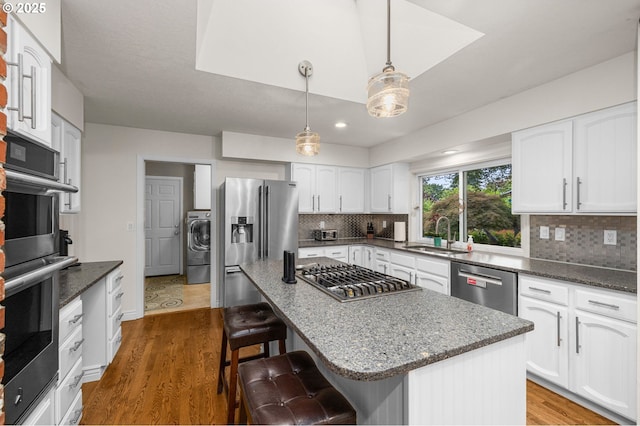 20060 SW Clarion St, Beaverton, OR 97003 - kitchen with appliances with stainless steel finishes, washer / dryer, a breakfast bar, backsplash, and wood finished floors