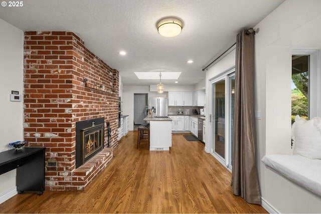20060 SW Clarion St, Beaverton, OR 97003 - kitchen with appliances with stainless steel finishes, white cabinets, wood finished floors, a brick fireplace, and a breakfast bar area