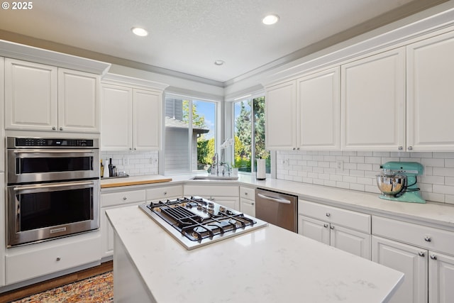 3753 NW Talamore Ter, Portland, OR 97229 - kitchen with stainless steel appliances, white cabinets, recessed lighting, decorative backsplash, and a center island