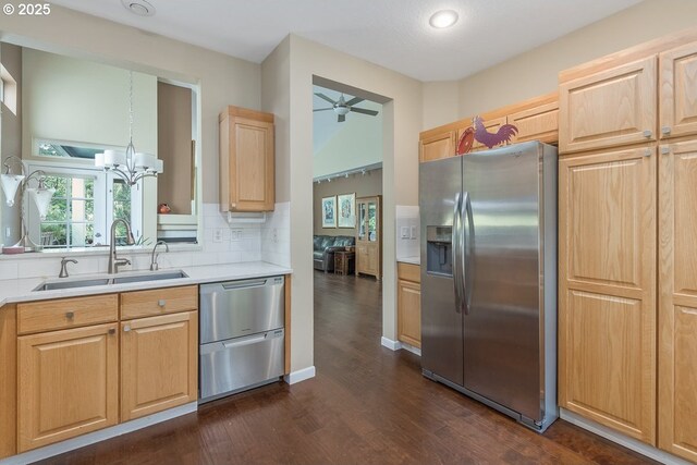 kitchen with decorative backsplash, dark wood finished floors, a sink, ceiling fan with notable chandelier, and stainless steel appliances