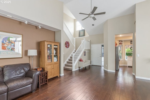 living area with a ceiling fan, wood finished floors, baseboards, high vaulted ceiling, and stairs