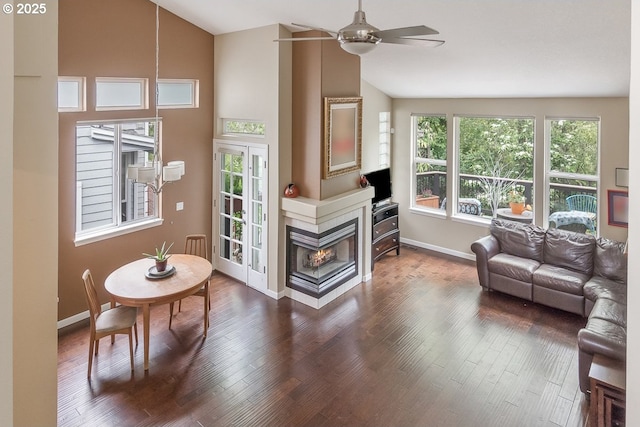 living room with ceiling fan, high vaulted ceiling, a multi sided fireplace, baseboards, and wood finished floors