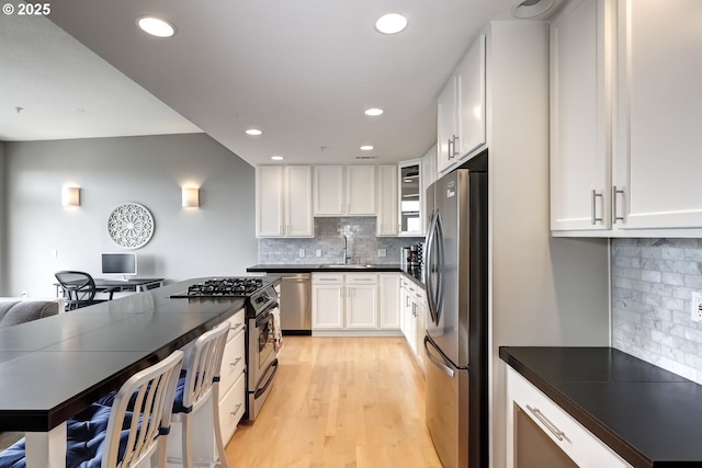 kitchen featuring appliances with stainless steel finishes, dark countertops, a sink, and light wood-style floors