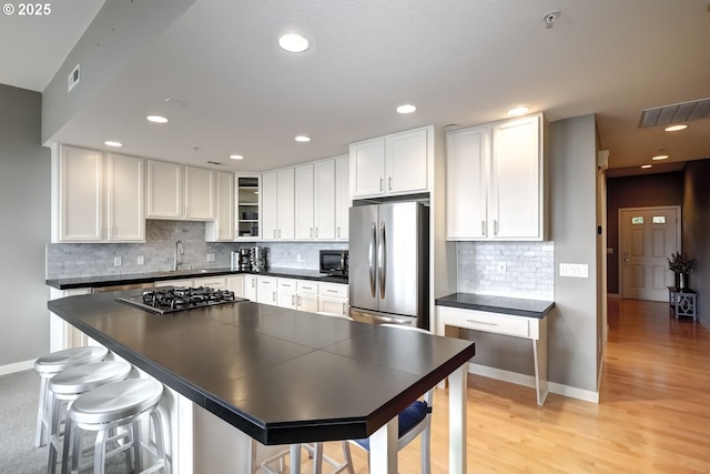 kitchen featuring a sink, white cabinets, appliances with stainless steel finishes, light wood finished floors, and dark countertops